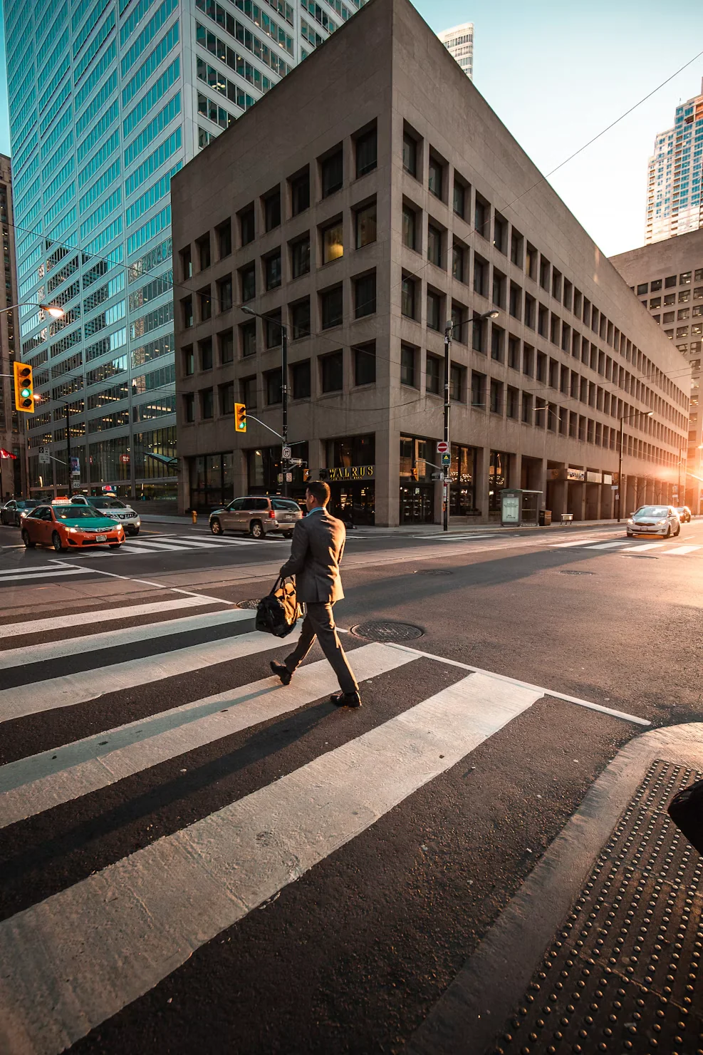 A person crossing a downtown street between office buildings at sunset